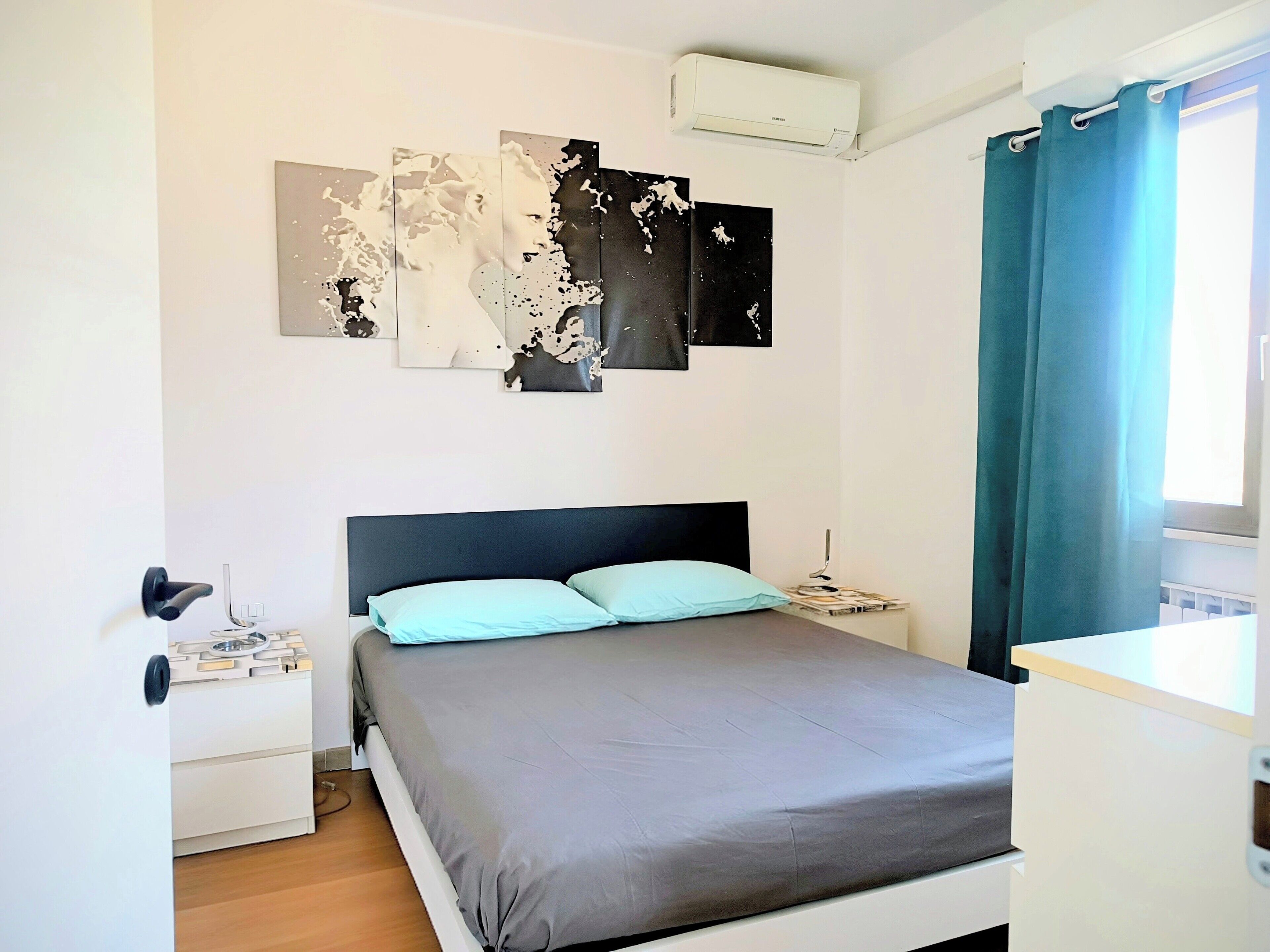 A bedroom with a bed, a nightstand, a wall-mounted air conditioner, and a window with curtains.
