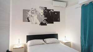 Een slaapkamer met een bed, witte wanden, een zwart hoofdeinde, een plafondairconditioner en een blauwgroen gordijn.