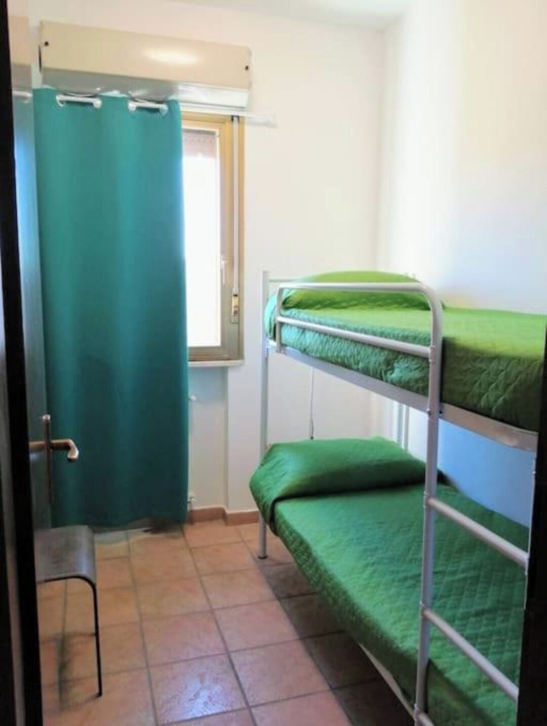 A bunk bed room with green bedding, a window, and a door with a curtain.