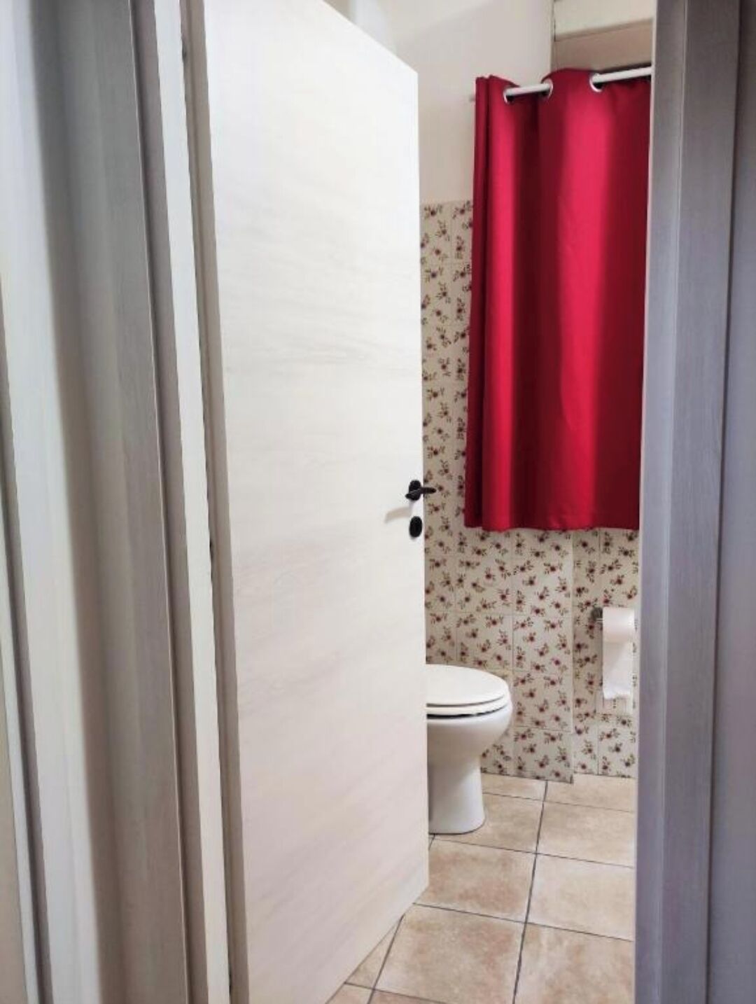 Une salle de bain avec des toilettes, un rideau de douche rouge et des carreaux à motifs floraux.
