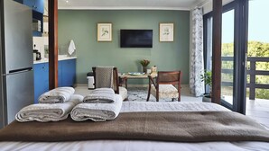Un dormitorio con cama, escritorio, silla, televisor y vistas al exterior.