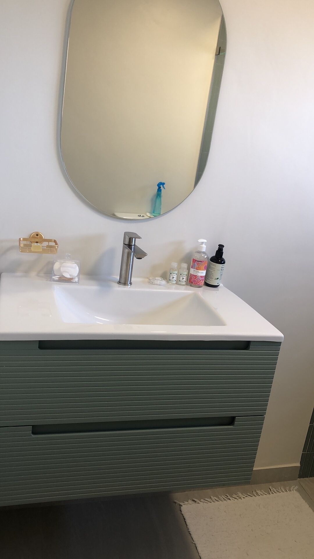 Une salle de bain avec un lavabo blanc, un miroir et des articles de toilette, notamment un distributeur de savon, un flacon de gel hydroalcoolique et un flacon de lotion.