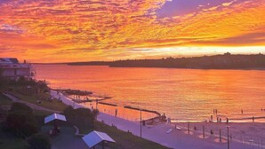 A waterfront view with a sunset, a promenade, and buildings along the shore. - Ocean view luxury 3 bedroom home with balcony (North Bondi)