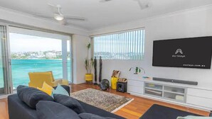 A modern living room with a large TV, comfortable seating, and a view of the ocean. - Ocean view luxury 3 bedroom home with balcony (North Bondi)