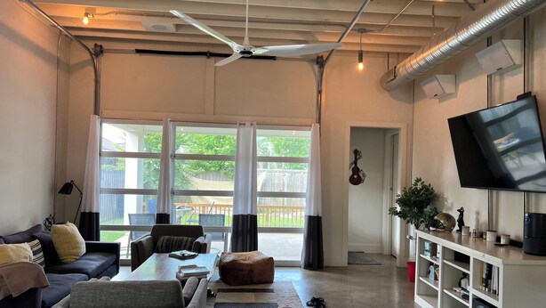A spacious living room with a large window, a ceiling fan, a flat-screen TV, and a built-in bookshelf.