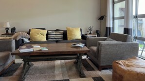 A modern living room with a dark sofa, striped cushions, a wooden coffee table, and a large window with curtains.