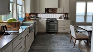 A modern kitchen with white cabinets, a brick backsplash, and a dining area with a bench.