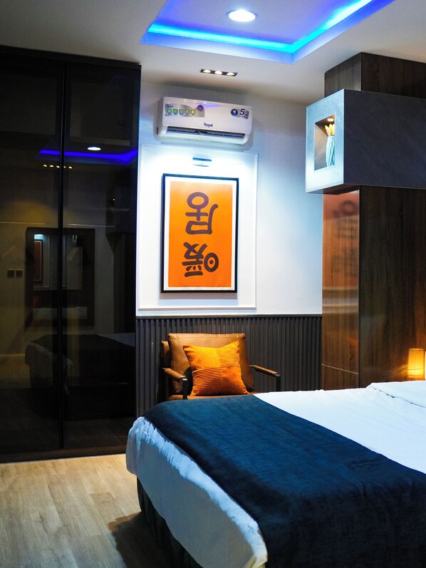 A modern hotel room with a bed, a wall-mounted air conditioner, a framed picture, and a television.