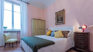 A bedroom with a bed, a chair, a dresser, a radiator, and a window with curtains. - Frejus Apartment by Wonderful Italy (Turin)