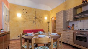 A dining area with a round table set for four, a red cushioned bench, and a kitchen with a modern stove and cabinets. - Frejus Apartment by Wonderful Italy (Turin)