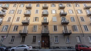A multi-story building with balconies, a central entrance, and a parking area with cars. - Frejus Apartment by Wonderful Italy (Turin)