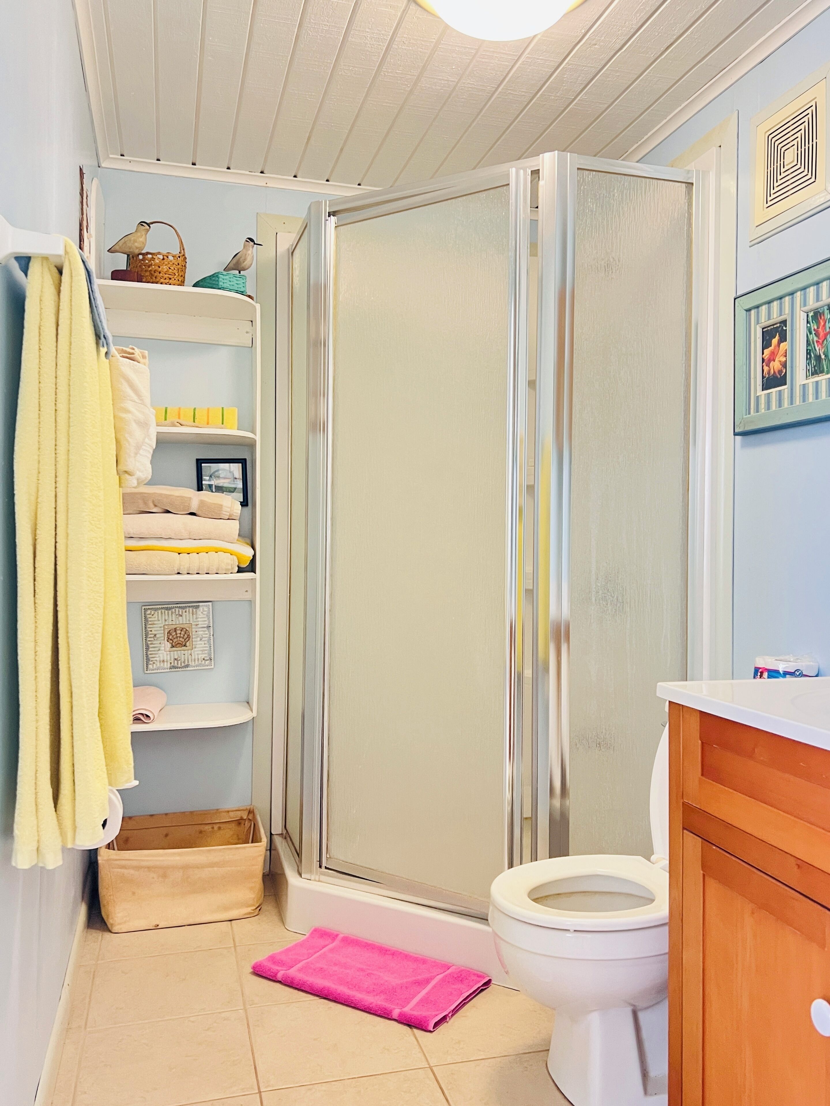 Une salle de bain avec une douche, des toilettes et un lavabo. On y trouve des serviettes et un panier sur les étagères.