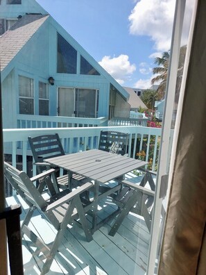 A balcony with a table and chairs, overlooking a blue house with a white railing. - 2-bed loft-style condo sleeps six, WiFi, pool, AC; walk to restaurants & beach (Frigate Bay)