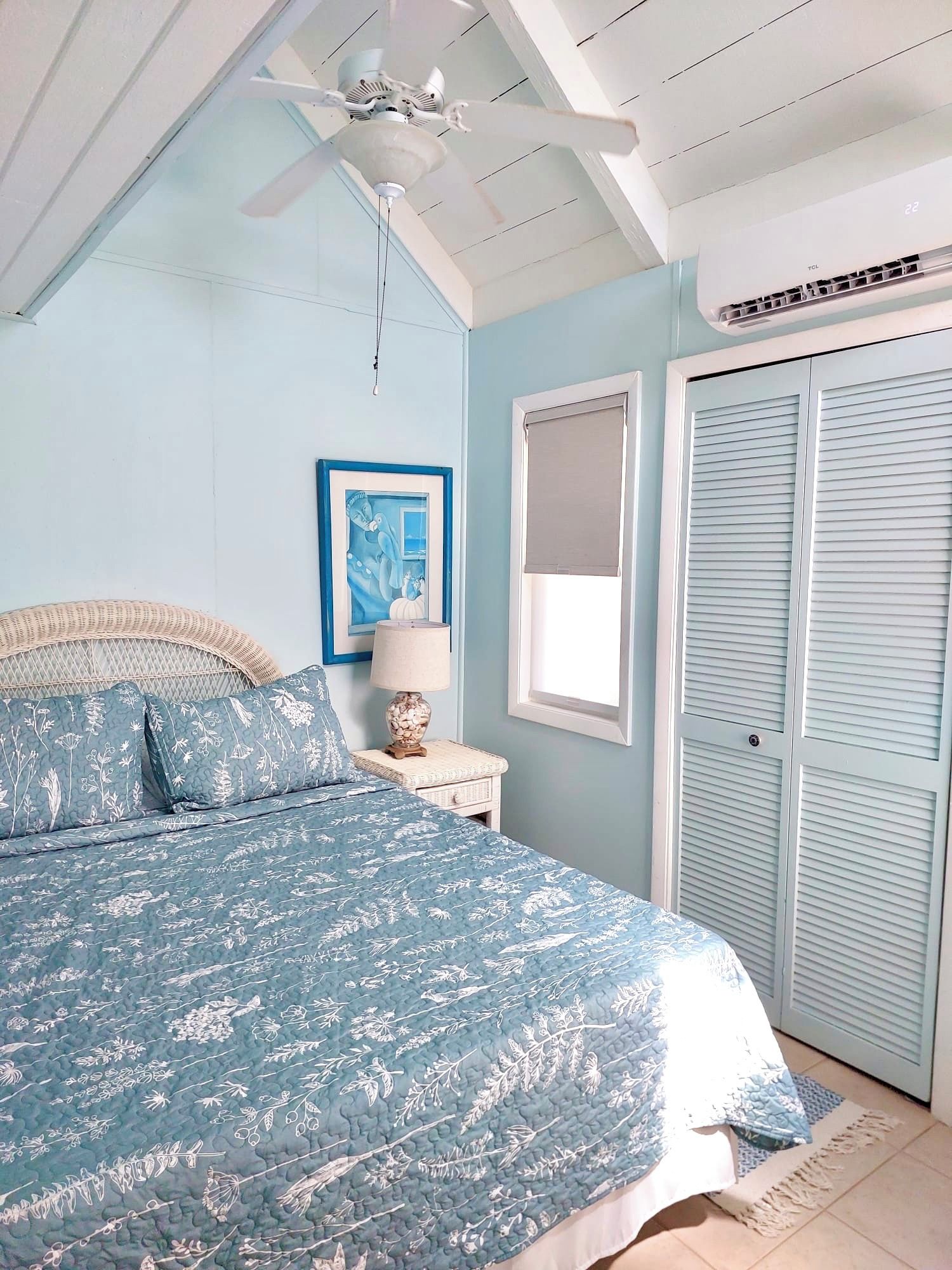 A bedroom with a bed, a ceiling fan, a window, and a door.
