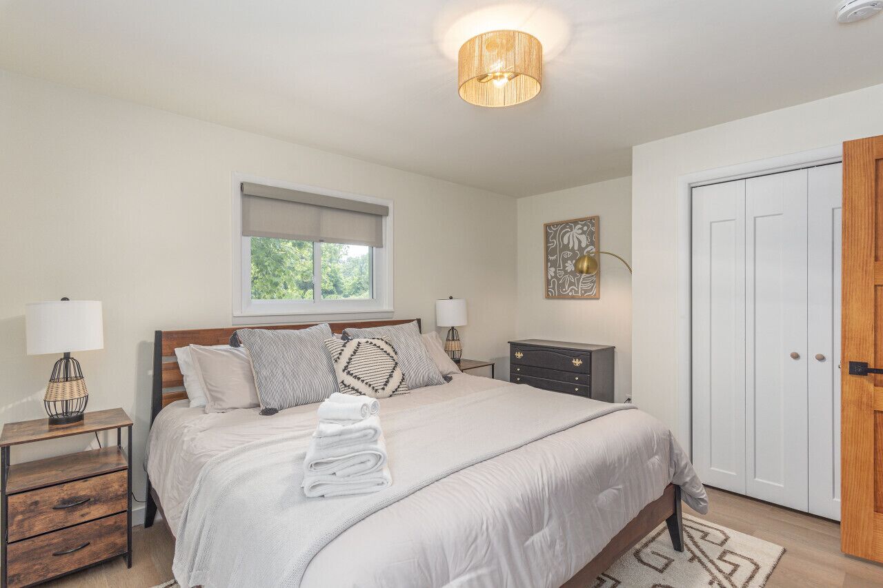 A bedroom with a bed, bedside tables, a lamp, a window, a door, and a wall decoration.