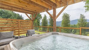 Ett område med ett bubbelbad, en träaltan och sittplatser, omgivet av ett trästaket och träd.