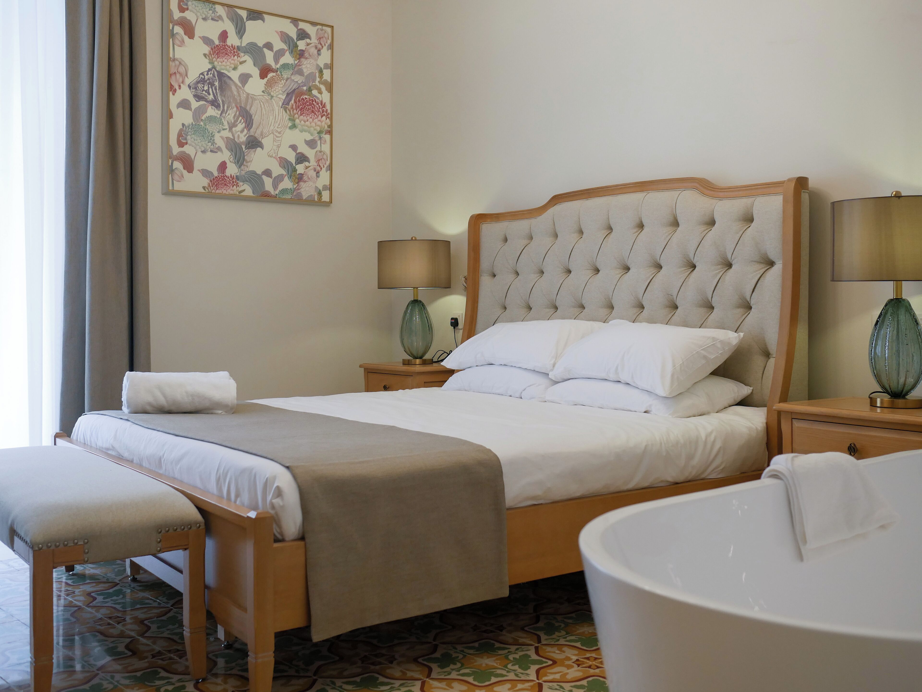 A neatly made bed with a tufted headboard, a bedside lamp, and a large mirror.