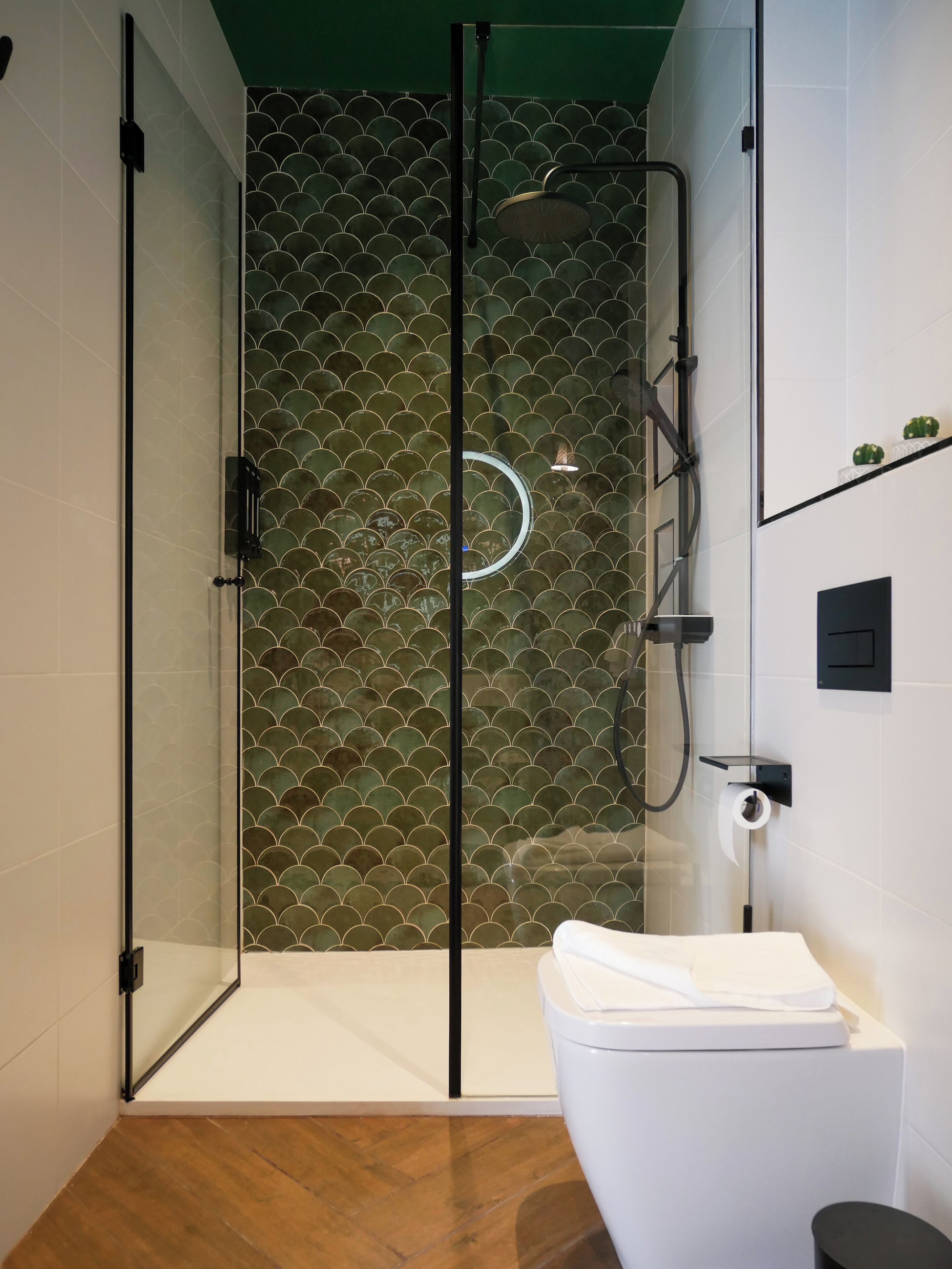 Un bagno moderno con doccia vetrata, vaso bianco e parete rivestita in piastrelle verdi.