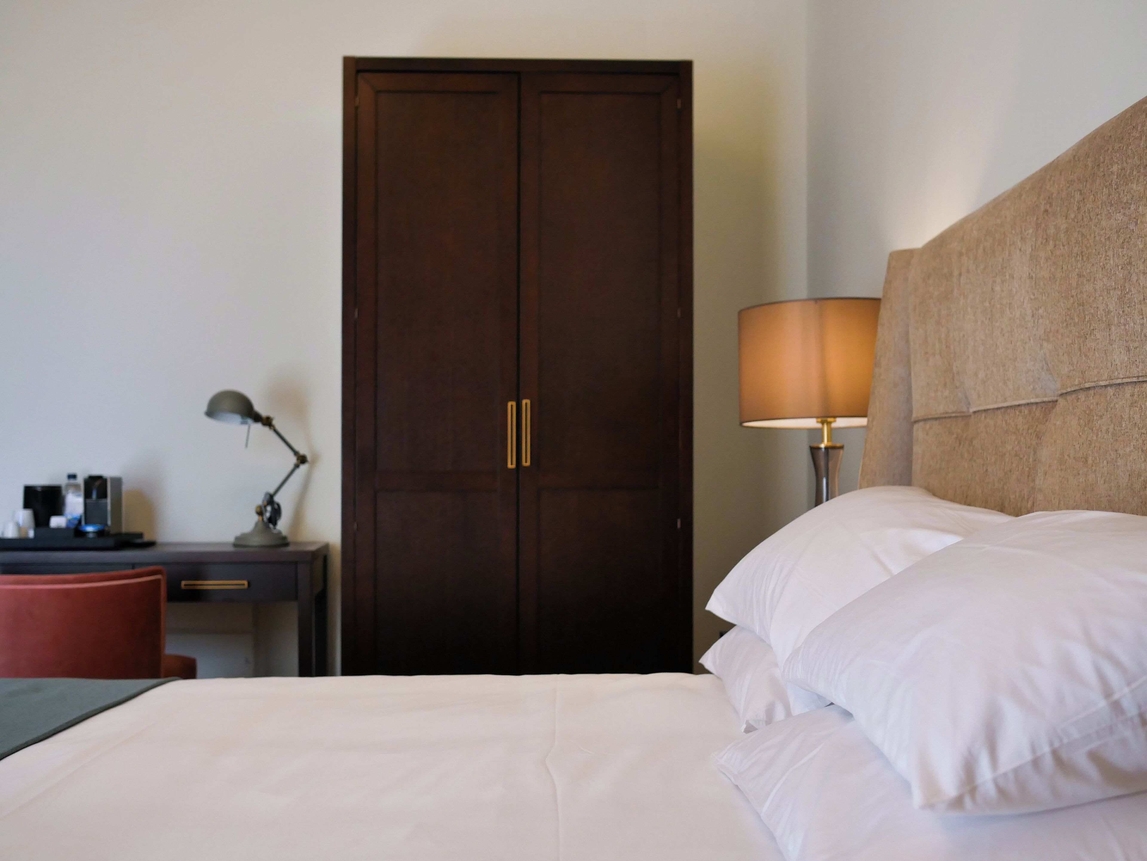 Een hotelkamer met een bed, een bureau met lamp en een kledingkast.