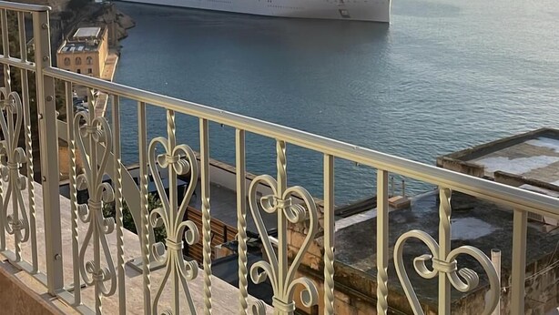 Una grande nave da crociera ormeggiata in un porto, con vista sullo splendido mare e un balcone con elaborate ringhiere in metallo.
