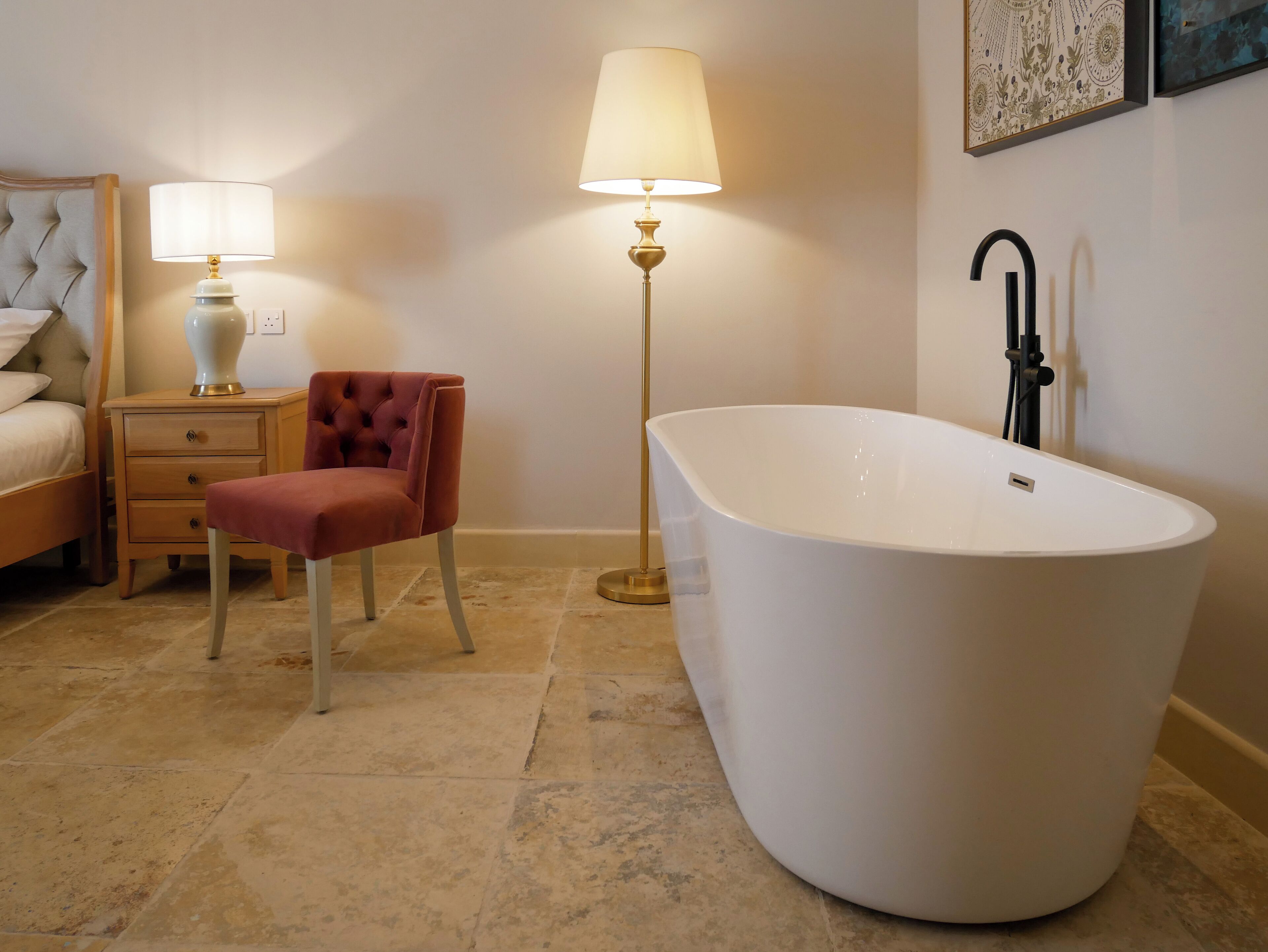 Une salle de bain moderne avec une baignoire sur pieds, une table de chevet avec une lampe, un fauteuil à capitons et un lit avec une tête de lit.
