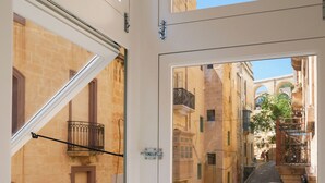 Un vicolo stretto fiancheggiato da edifici, cielo azzurro e una finestra con balcone in metallo.