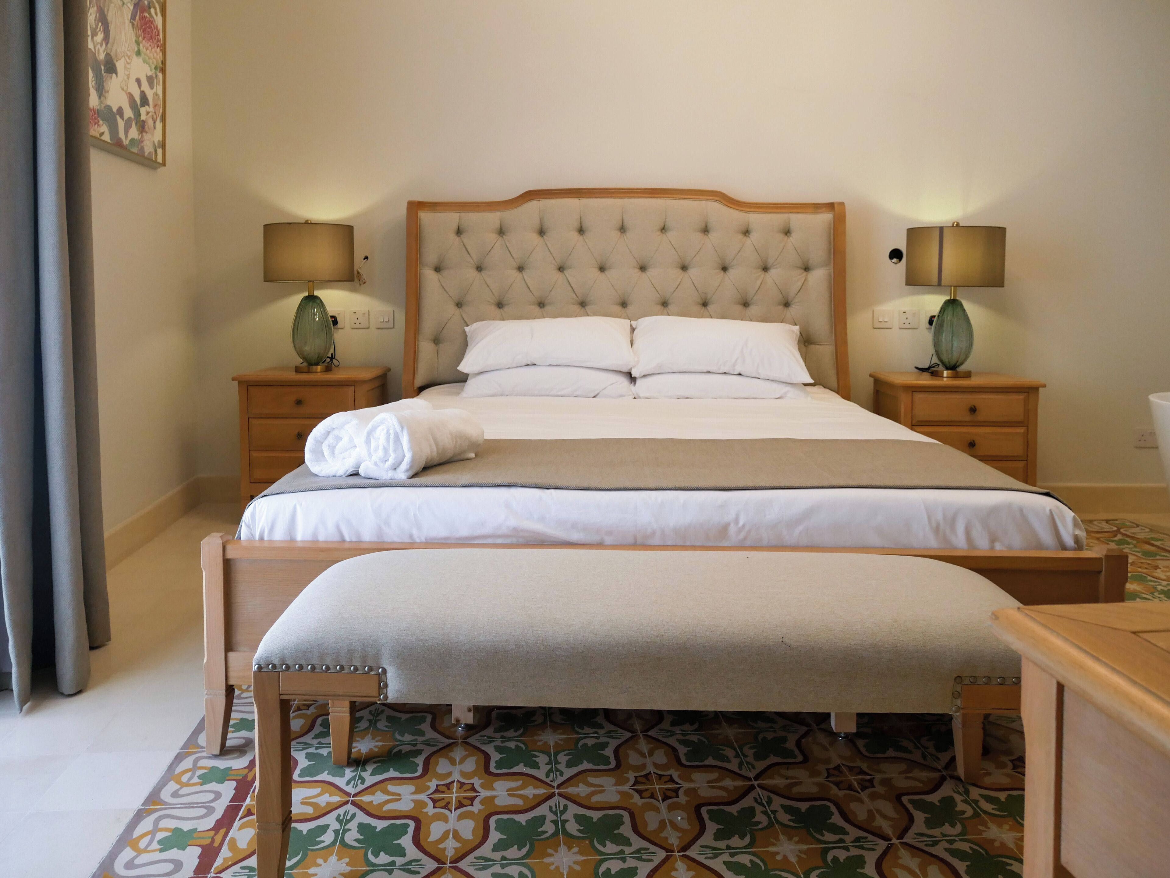 A neatly made bed with white linens, a beige headboard, and two bedside tables with lamps.