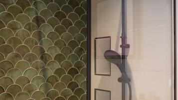 A glass-enclosed shower with a modern design, featuring a curved showerhead and a handheld shower attachment.