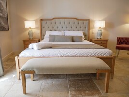 Un dormitorio ordenado con una cama grande, dos mesitas de noche con lámparas, un banco y una silla roja.