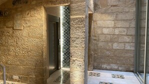 Un corridoio con pareti in pietra, un ascensore moderno e piastrelle del pavimento a motivi.