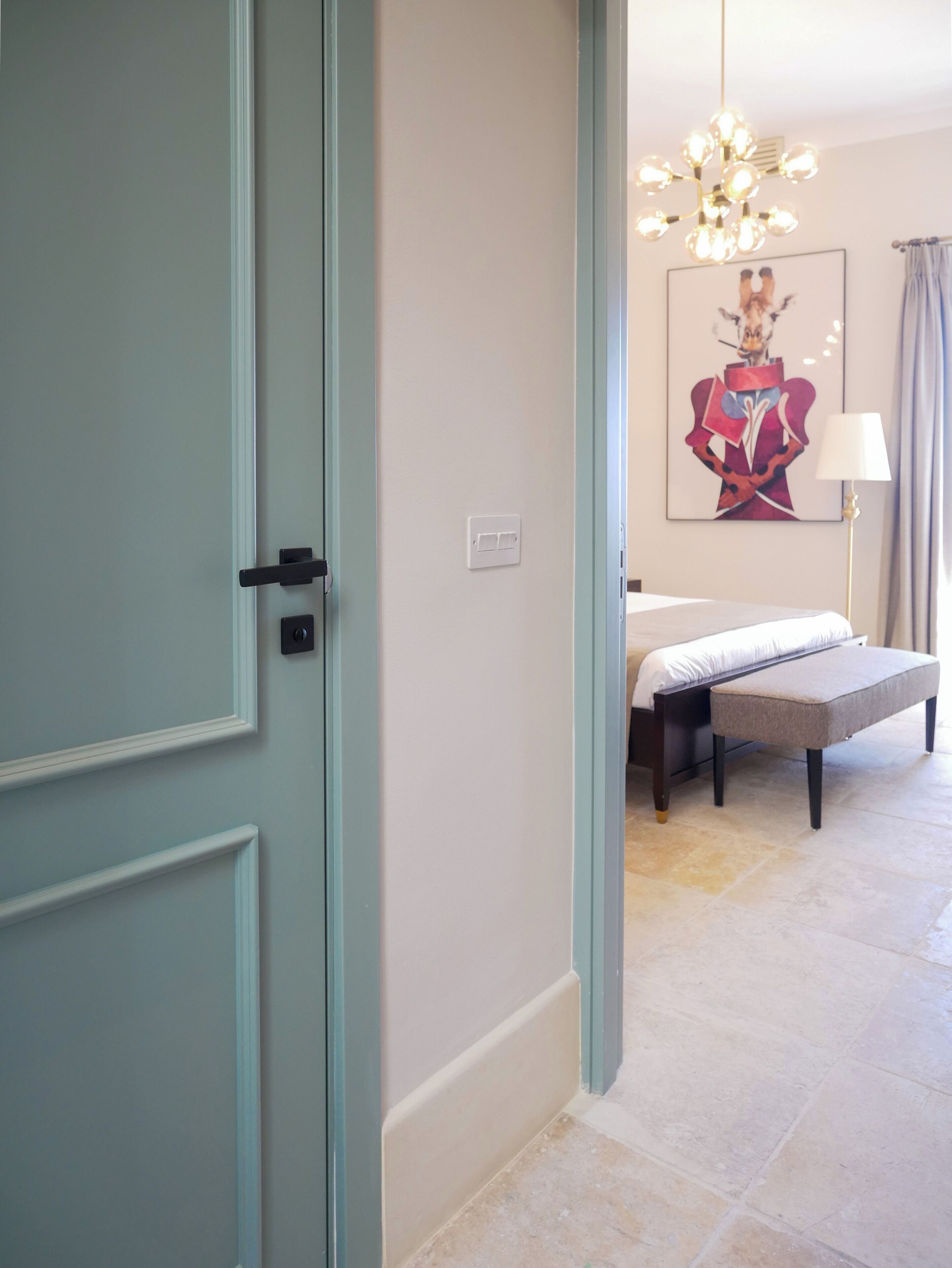 Un dormitorio con cama, banca, candelabro y obras de arte en la pared.