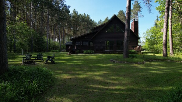 A cabin surrounded by a forest with a deck and outdoor seating.