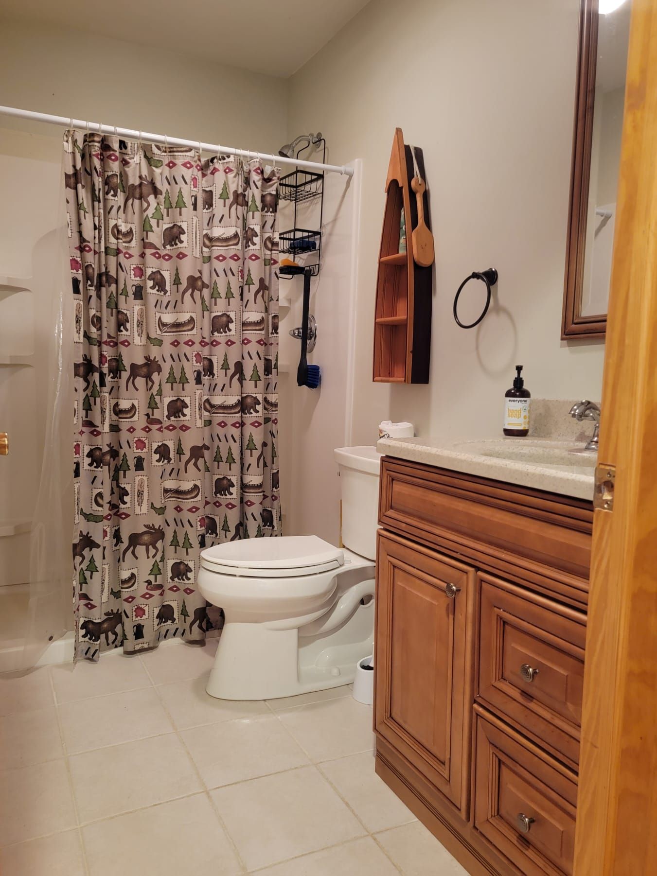 A bathroom with a toilet, a shower curtain with animal prints, a wooden cabinet, and a mirror.