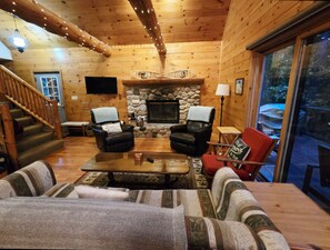 Interior acollidor d'una cabana amb una llar de pedra, butaques de cuir, un sofà i una taula de dinar.
