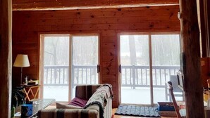 L’intérieur d’un chalet accueillant, avec un plafond en bois, un canapé, une table avec une lampe et de grandes fenêtres.