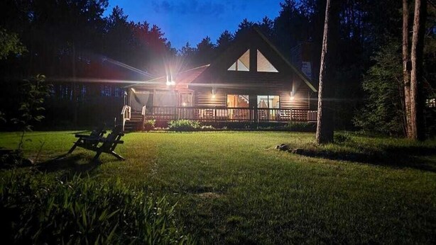 Une cabane avec une véranda, un fauteuil de jardin et un éclairage extérieur suffisant au crépuscule.