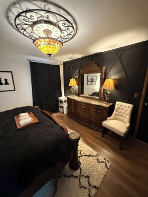 Ein Schlafzimmer mit Bett, Schminktisch, Stuhl, Spiegel und einer Chandelier.
