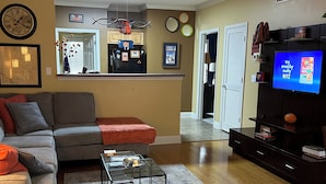 A living room with a grey sofa, a coffee table, a TV, and a ceiling fan. - Auburn First Floor Condo. Walking Distance To Jordan Hare and Auburn Arena (Auburn)