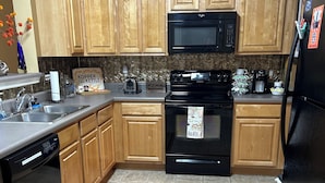 A kitchen with wooden cabinets, a black microwave, a stove, and a refrigerator. - Auburn First Floor Condo. Walking Distance To Jordan Hare and Auburn Arena (Auburn)