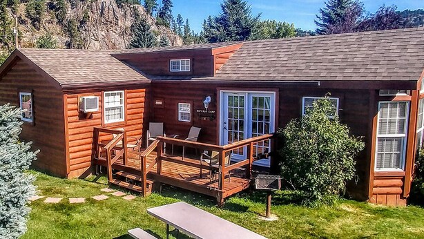 Una cabaña de troncos con terraza, asientos exteriores y una mesa de picnic.
