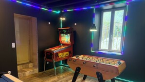 Una habitación con mesa de fútbol de mesa, máquina de pinball e iluminación LED a lo largo de las paredes.
