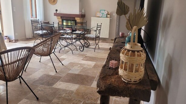Un comedor con sillas de mimbre y una mesa de madera rústica, un radiador y objetos decorativos en la pared.