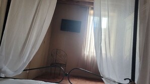Una habitación con una cama, una silla y una ventana con cortinas traslúcidas.