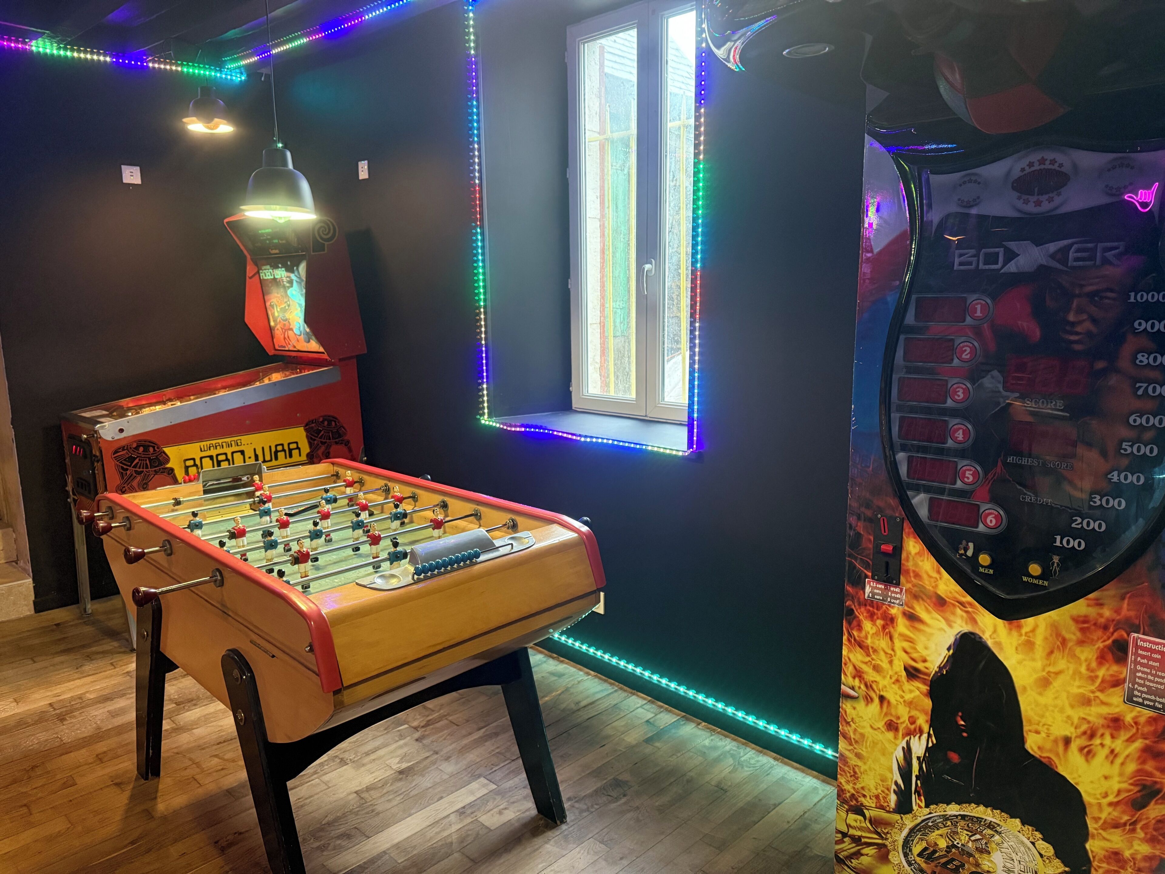 Una habitación con mesa de futbolín, ventana con vistas y luces LED de colores.