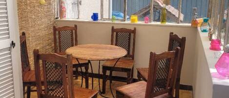 Une terrasse couverte avec une table et des chaises en bois, un mur en paille et une vue sur un bâtiment traditionnel.