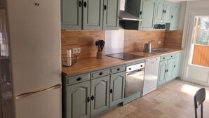 Una cocina con gabinetes verde claro, encimera de madera, pileta de acero inoxidable y lavavajillas blanco.