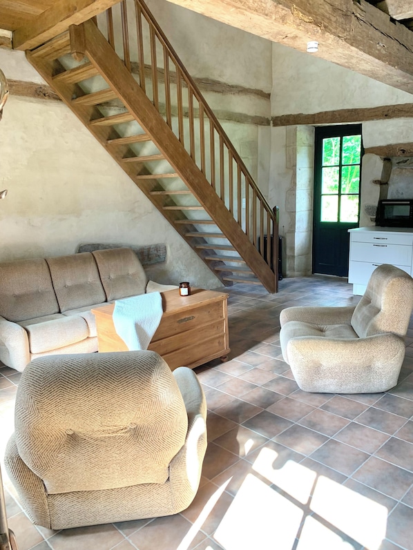 A rustic interior with a wooden staircase, a sofa, a chair, and a small wooden cabinet. - Gite Simple et Authentique, au Calme Pour les Amoureux de la Nature (Bazoges-en-Pareds)