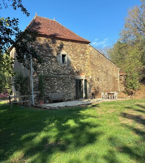A stone building with a tiled roof, a bench, and a table set outside.