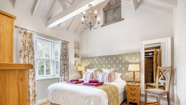 A bedroom with a large bed, a wooden chair, a nightstand, a chandelier, and a window with curtains. - 2 bedroom accommodation in Burgh Le Marsh (Burgh Le Marsh)