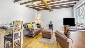 A living room with a fireplace, leather sofas, wooden flooring, and exposed wooden beams. - 2 bedroom accommodation in Burgh Le Marsh (Burgh Le Marsh)